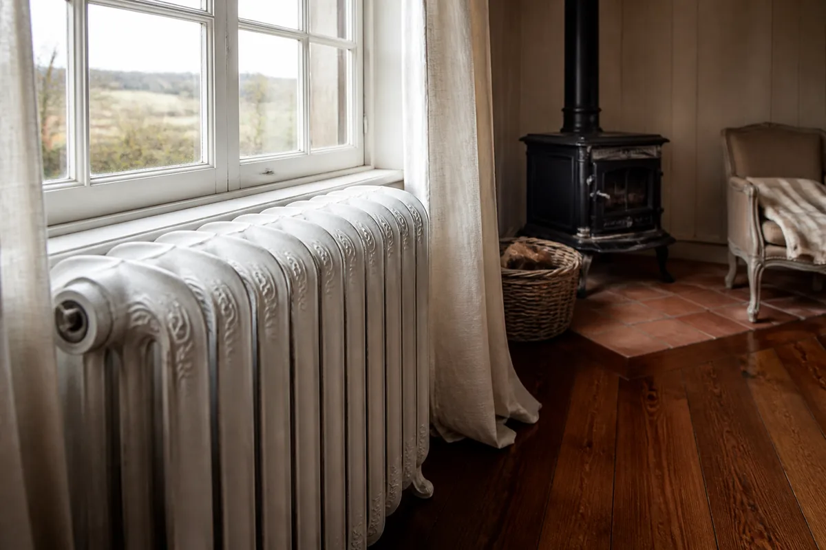 Radiateur en fonte ancien sous une fenêtre d'une maison limousine, robinet thermostatique en laiton au premier plan